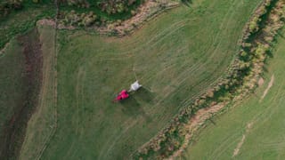 Aerial view of a red tractor towing a Tow and Fert Multi 2800 sprayer along a steep grassy hillside.