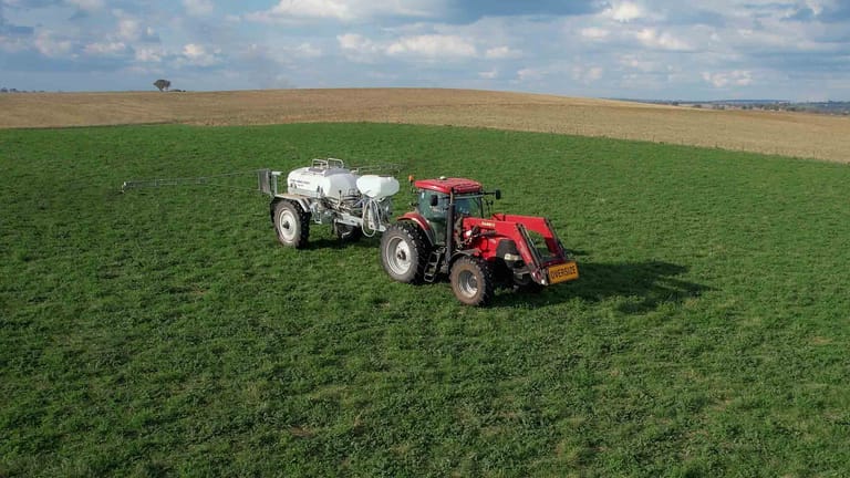 Aerial view of a red tractor towing a Tow and Fert MultiCrop 4000 sprayer across a green field, with spray booms extended.